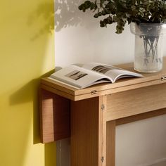 an open book on a wooden table next to a vase with green plants in it