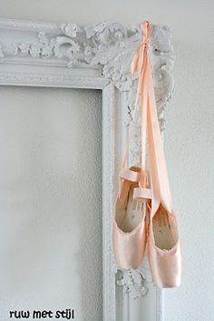 two pairs of pink ballet shoes hanging from a white frame