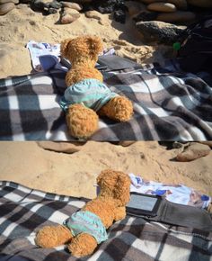 a teddy bear laying on top of a blanket in the sand next to a pile of rocks