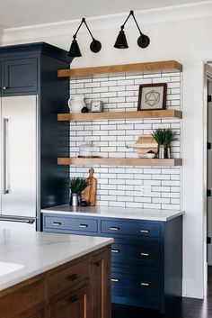 a kitchen with blue cabinets and white subway backsplash, wood shelves and hanging potted plants