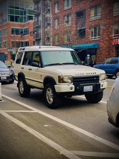 an suv is driving down the street in front of other cars and people walking on the sidewalk