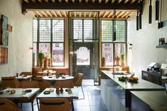 an empty restaurant with tables and chairs in front of large windows, along with potted plants on the wall