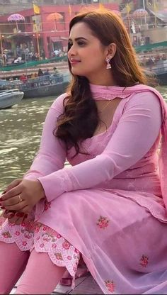 a woman in pink dress sitting on the edge of a boat looking off into the distance