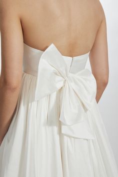 a woman wearing a white dress with a big bow on the back