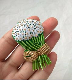 a hand holding a green and white brooch with daisies on it's side