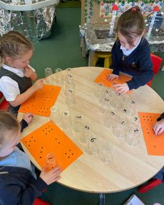 three children sitting at a table playing with plastic cups and orange letters on them,