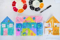 children's artwork displayed on white surface with markers and pencils, including paper houses