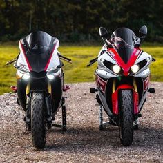 two motorcycles are parked next to each other on the gravel road in front of some trees