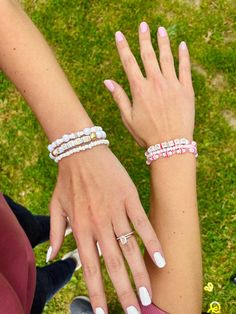 two women's hands holding onto each other on the grass with their nails painted pink and white