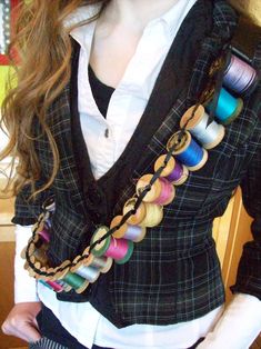 a woman with long hair wearing a black jacket and colorful thread spools on it's lapel