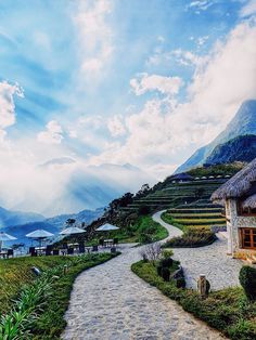 a pathway leading to a house on the side of a hill with mountains in the background