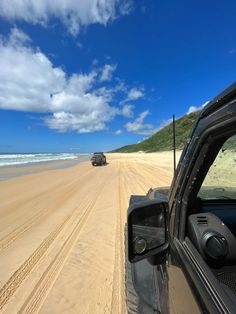 a car driving on the beach next to the ocean under a blue sky with white clouds