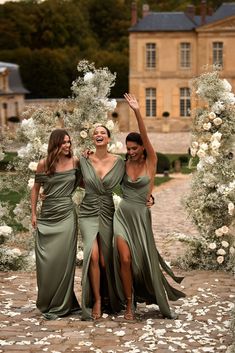 three bridesmaids in green dresses standing under an arch with white flowers on it