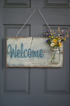 a sign that says welcome hanging on a door with flowers in a mason jar attached to it