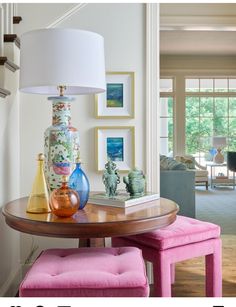 a table with two vases on top of it and a pink ottoman underneath the table