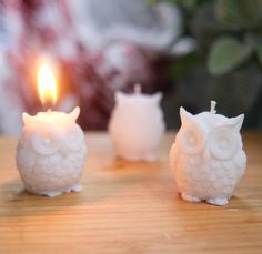 three white candles sitting on top of a wooden table next to an owl figurine