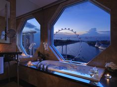 a bathroom with a large window overlooking the water and ferris wheel in the background at dusk