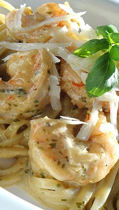 pasta with shrimp, onions and herbs on a white plate next to a fork in a glass container