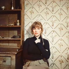 a woman sitting in front of a wooden desk next to a wallpapered wall