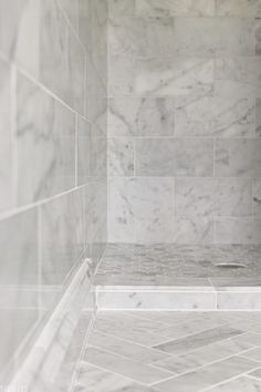 a marble tiled shower stall in a bathroom with white tile flooring and gray tiling