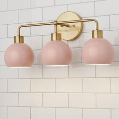 three light bathroom fixture with pink glass shades on white brick wall and gold fittings