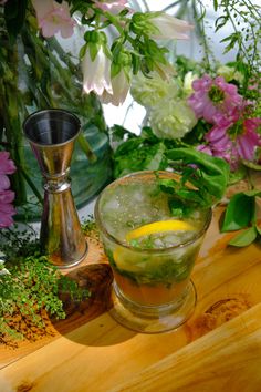 a glass filled with ice and lemon sitting on top of a wooden table next to flowers