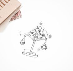 a drawing of a scale with flowers on it next to a book that reads libra