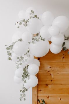 white balloons and greenery are hanging from the ceiling over a wood paneled wall