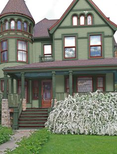 a large green house with many windows and flowers in the front yard, on a cloudy day