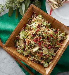 a wooden bowl filled with salad on top of a green cloth next to a fork and knife