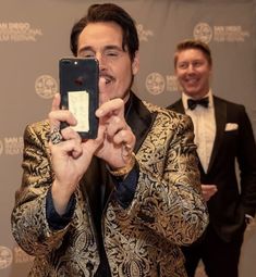 a man in a tuxedo taking a selfie with his cell phone at an event