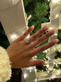 a woman's hand with a ring on it and christmas lights in the background