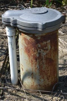 an old rusted metal trash can sitting in the middle of some grass and dirt