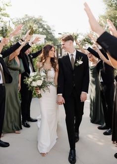 a bride and groom walking through a group of people holding their hands up in the air