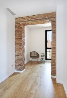 an empty room with a chair and brick wall in the corner, next to a window