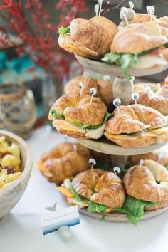 sandwiches and croissants are displayed on three tiered trays with little eyes