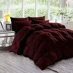 a bed with red comforter and pillows in a room next to a white table