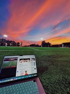 an open laptop computer sitting on top of a green grass covered field next to a soccer field