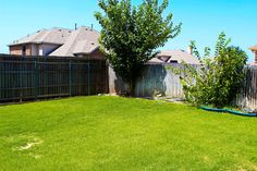 a backyard with green grass and trees in the back yard, next to a fence