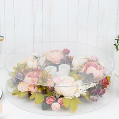 a glass bowl filled with flowers on top of a white table next to two candles