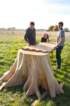 two men standing next to a wooden table in the middle of a field with grass