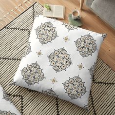 a white floor pillow with an intricate pattern on it and a cup of coffee next to it