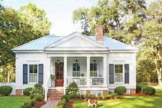 a white house with blue shutters and a dog in the front yard on a sunny day