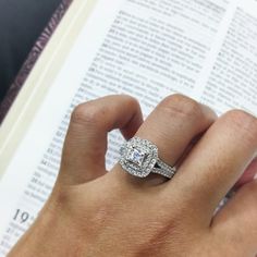 a person is holding an open book with a diamond ring on their finger and reading the bible