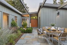 an outdoor dining area with wooden chairs and table in front of two gray building's