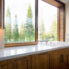 a kitchen with wooden cabinets and white counter tops next to a large window that looks out onto the woods