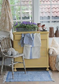 a yellow dresser sitting next to a window filled with potted plants and other items