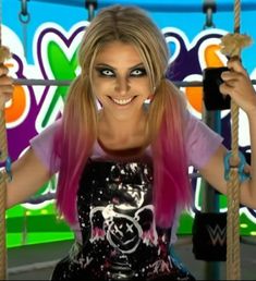 a woman with pink hair and makeup is on a swing in front of a colorful background