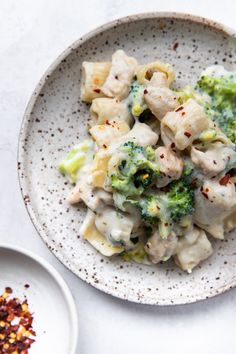 a white plate topped with broccoli and dumplings next to a bowl of seasoning