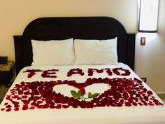 a bed with white sheets and red rose petals in the shape of a heart